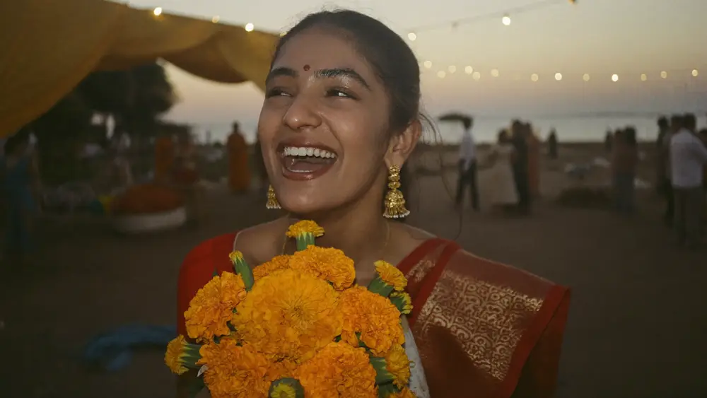 A laughing bride holding marigolds, the flowers sharp in front of a softly blurred venue