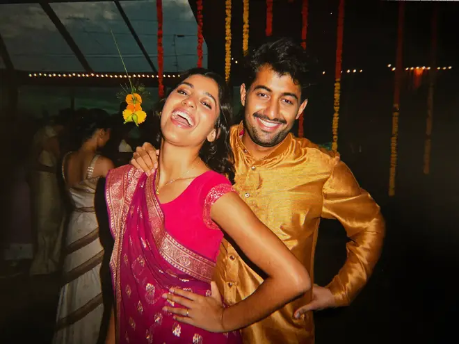 A couple at a sangeet settling into a pose together, both laughing